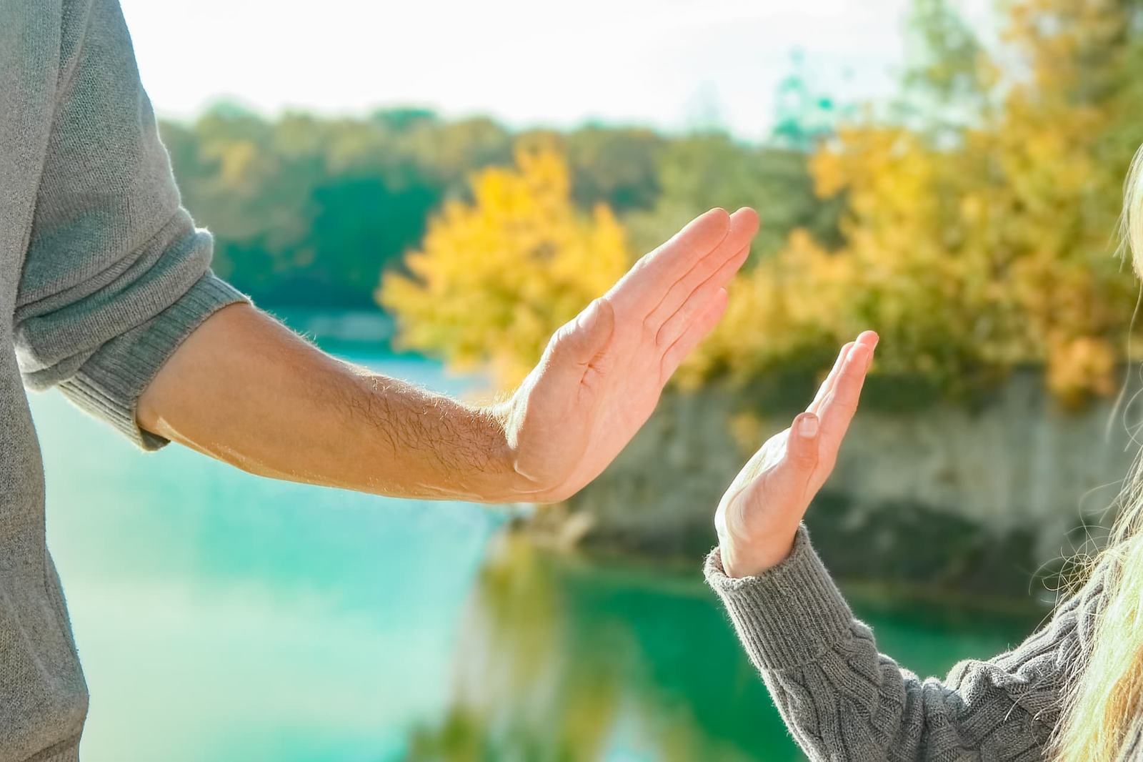 Manos de un adulto y una niña frente a un lago al sol