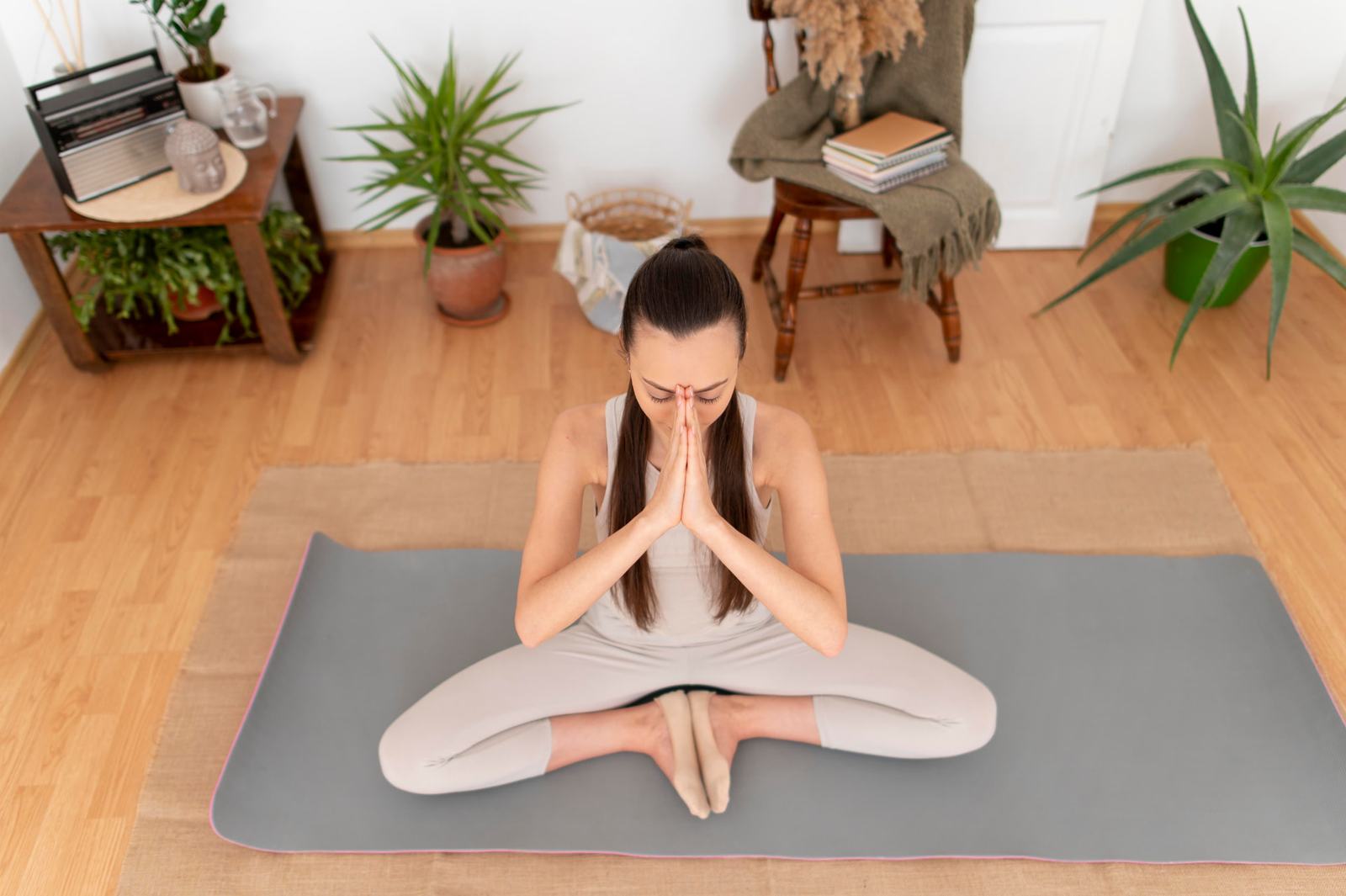 Mujer meditando en su casa sobre una esterilla, rodeada de plantas