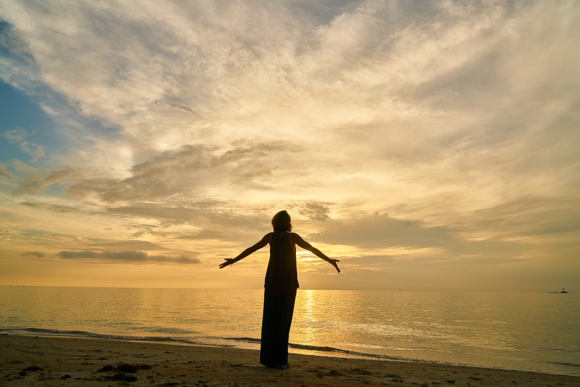 Mujer con los brazos abiertos frente al mar al atardecer